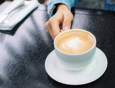 bir kadının elinde bir kafe veya restoranda siyah masada köpük krema ile kapuçino kahve espresso beyaz fincan