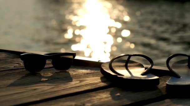 Vakantie op het strand met slippers en zonnebrillen bij zonsondergang. — Stockvideo