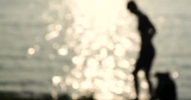 Deodaklanmış, bulanık ön plan Kadın sahilde gün batımında köpeğini oynar , Yavaş hareket 4k