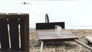 Ahşap Şezlong ve plajda boş bardak, arka planda kayaker kürek 4k