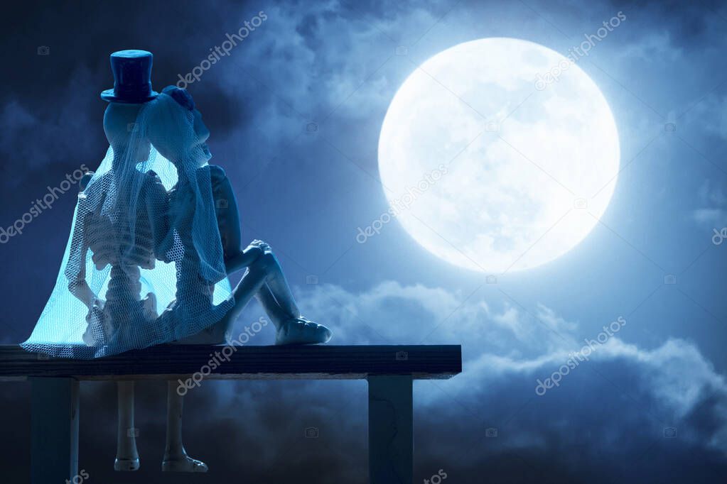 Dramatic photo illustration of a nighttime sky with brightly lit clouds as a large, full, Blue Moon greats a lovely couple of skeleton lovers on Halloween. 