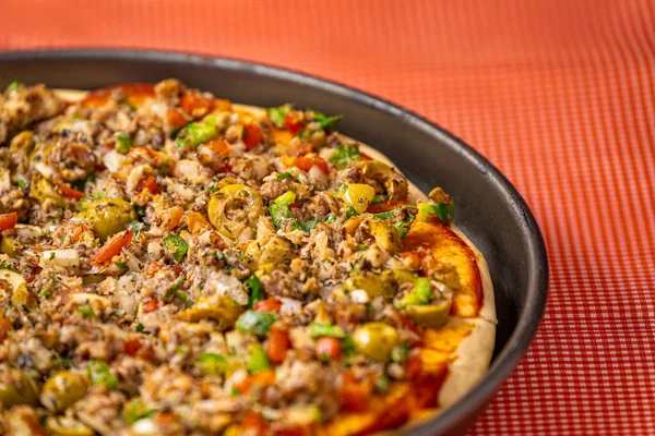 A tasty sardine pizza with olives, tomatoes and onions. Home made with fresh, soft dough, in a round shape and on top of the checkered tablecloth.