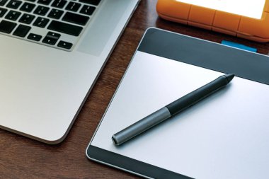 Bilgisayarın siyah ekranının görüntülenmesi, evde çalışacak bir cihaz, araştırma, ajanda, HD, cep telefonu, grafik tableti, kulaklık ve USB bellek. Tahta bir ofis masasının üstünde..