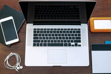 Bilgisayarın siyah ekranının görüntülenmesi, evde çalışacak bir cihaz, araştırma, ajanda, HD, cep telefonu, grafik tableti, kulaklık ve USB bellek. Tahta bir ofis masasının üstünde..