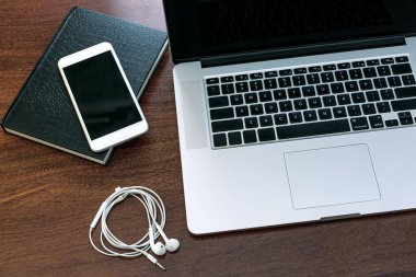 Bilgisayarın siyah ekranına bakmak, evde çalışmak için bir cihaz, araştırma, ajanda, HD, cep telefonu, kulaklık ve USB bellek. Tahta bir ofis masasının üstünde..