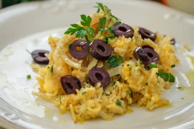 Patates pipetli, karışık yumurtalı ve koyu zeytinli lezzetli bir morina balığı. Tahta bir masada, sarımsak, soğan, maydanoz ve tarifin diğer malzemeleriyle..