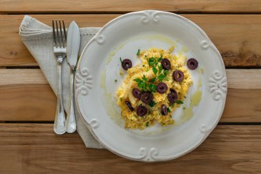 Patates pipetli, karışık yumurtalı ve koyu zeytinli lezzetli bir morina balığı. Tahta bir masada, sarımsak, soğan, maydanoz ve tarifin diğer malzemeleriyle..