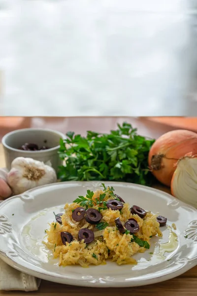 Patates pipetli, karışık yumurtalı ve koyu zeytinli lezzetli bir morina balığı. Tahta bir masada, sarımsak, soğan, maydanoz ve tarifin diğer malzemeleriyle..