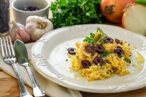 Patates pipetli, karışık yumurtalı ve koyu zeytinli lezzetli bir morina balığı. Tahta bir masada, sarımsak, soğan, maydanoz ve tarifin diğer malzemeleriyle..