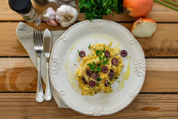 Patates pipetli, karışık yumurtalı ve koyu zeytinli lezzetli bir morina balığı. Tahta bir masada, sarımsak, soğan, maydanoz ve tarifin diğer malzemeleriyle..