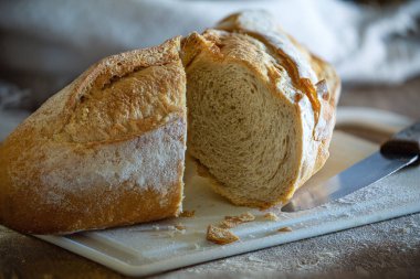 Taze, gevrek bir İtalyan ekmeği, beyaz bir tahta üzerinde ahşap bir masa ve buğday unu..