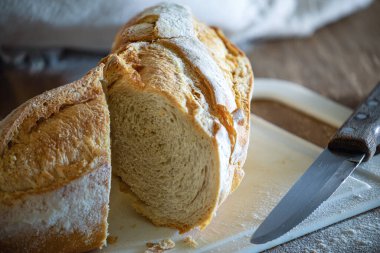 Taze, gevrek bir İtalyan ekmeği, beyaz bir tahta üzerinde ahşap bir masa ve buğday unu..