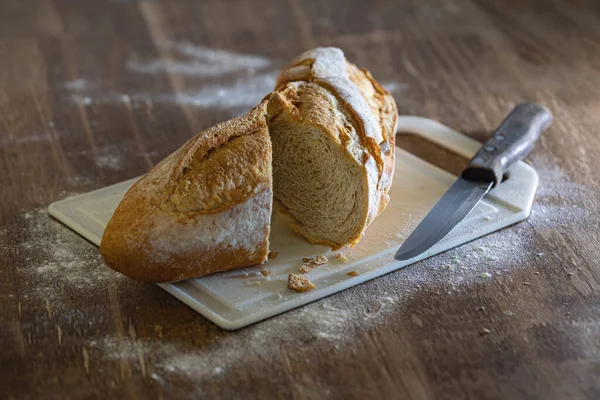 一块新鲜而脆的意大利面包 放在木制桌子上的一块白色切菜板上和小麦粉上 — 图库照片
