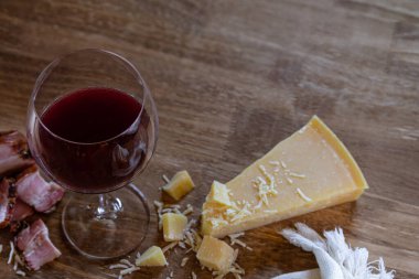 Aperatifler, parmesan peyniri ve pastırma parçaları eşliğinde ahşap bir masada bir bardak kırmızı şarap. Boş metin alanı olan bir düzen.