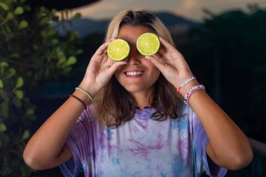 Koyu bir arka planda poz veren güzel, inanılmaz mutlu bir genç kadının görüntüsü. Elinde limon ve portakallarla kameraya bakıyor..