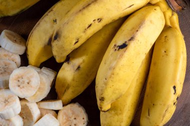 Bir demet muz, kasede dilimlenmiş muz ve tahta tahtada.