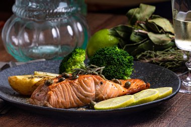 Bir parça kızarmış somon ızgara limon biberi ve brokoli ile birlikte koyu bir tabakta tuz. Ahşap arkaplan