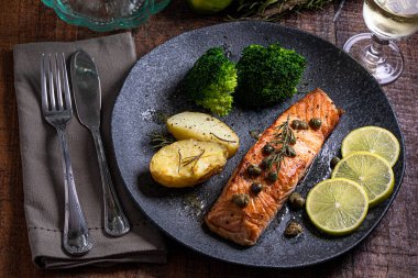 Bir parça kızarmış somon ızgara limon biberi ve brokoli ile birlikte koyu bir tabakta tuz. Ahşap arkaplan
