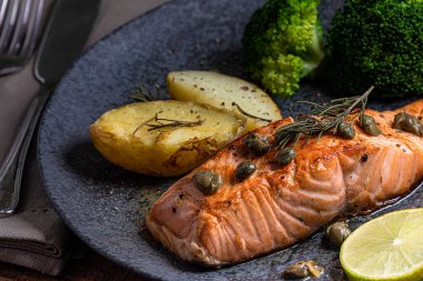 Bir parça kızarmış somon ızgara limon biberi ve brokoli ile birlikte koyu bir tabakta tuz. Ahşap arkaplan