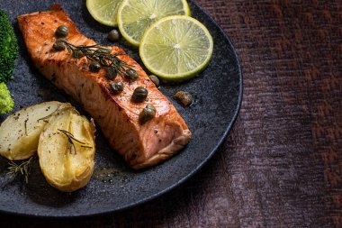 Bir parça kızarmış somon ızgara limon biberi ve brokoli ile birlikte koyu bir tabakta tuz. Ahşap arkaplan