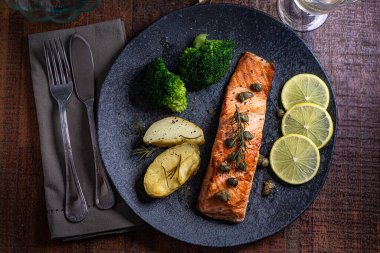 Bir parça kızarmış somon ızgara limon biberi ve brokoli ile birlikte koyu bir tabakta tuz. Ahşap arkaplan