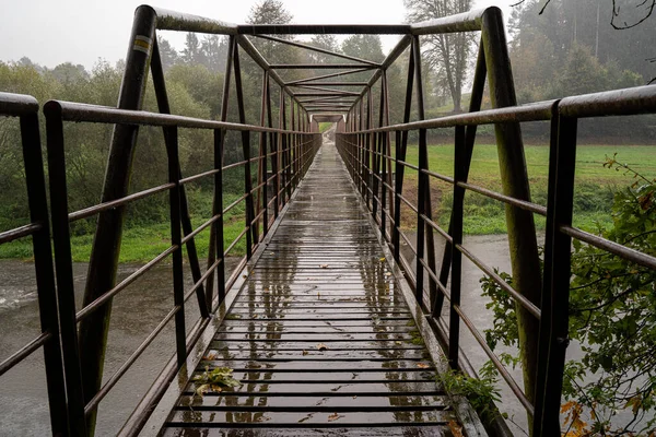 Stalowy most z drewnianą ścieżką spacerową. Przeprawa przez rzekę przy złej pogodzie. — Zdjęcie stockowe