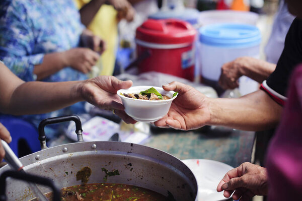 Бедные люди получают еду из пожертвований: бездомным помогают с продовольствием, облегчают голод: добровольцы дают пищу бедным людям в отчаянной нужде
