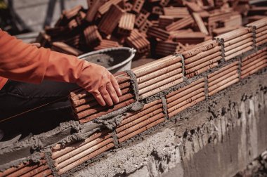 Bir inşaatçı bir evin üzerine duvar örmek için kil tuğla döker..