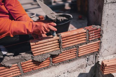 Bir inşaatçı bir evin üzerine duvar örmek için kil tuğla döker..