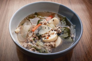 Tofu, yumurta, kıyma, lahana, havuç, soğan ve üzerine siyah beyaz susam tohumları serpiştirilmiş şeffaf çorba..