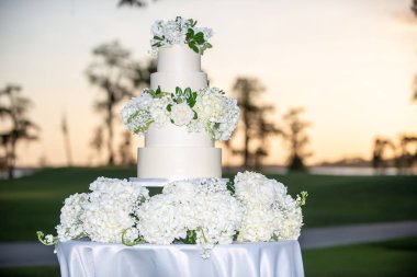 Beyaz beş katlı düğün pastası, açık havada beyaz güller.