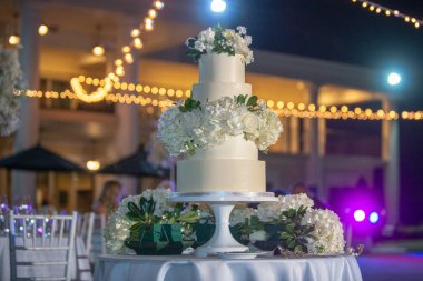 Beyaz beş katlı düğün pastası, açık havada beyaz güller.