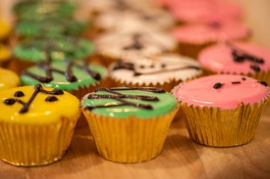 Kekler çeşitli renkler ve tatlar altın bardaklarda ahşap kesiminde.