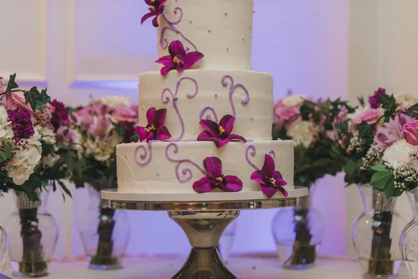 White three tier wedding cake with purple flowers decor