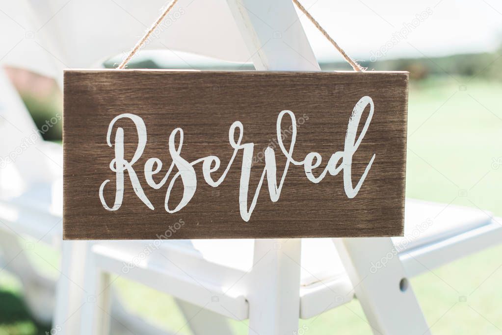 wood reserved seating sign hanging on white chairs outdoors