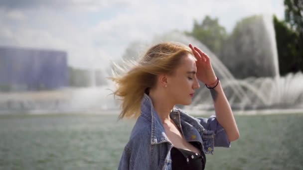 Bella ragazza bionda caucasica che cammina vicino alla fontana del fiume — Video Stock