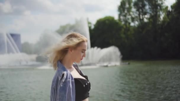 Bella ragazza bionda caucasica che cammina vicino alla fontana del fiume — Video Stock