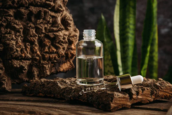 Cosmetisch serum in een glazen fles met een pipet op een donkere achtergrond met natuurlijke materialen. — Stockfoto