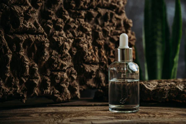 Cosmetisch serum in een glazen fles met een pipet op een donkere achtergrond met natuurlijke materialen. — Stockfoto