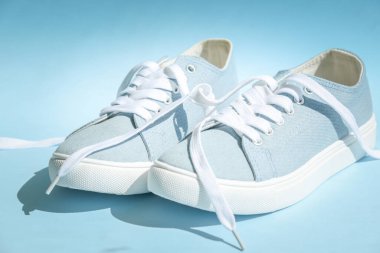 Açık mavi arka planda beyaz bağcıklı mavi spor ayakkabılar..