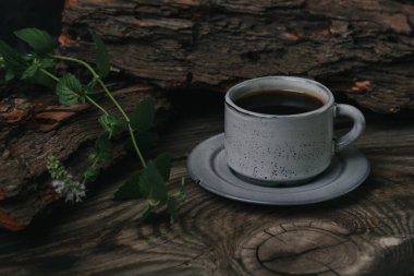 Koyu arkaplanda, ahşap bir masada bir fincan espresso kahvesi. Yakınlarda taze nane şekeri var..