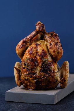 Güzel bir altın kahverengi kabuk ile ahşap bir tahta üzerinde baharat, otlar ve limon ile Fırında fırında tavuk.