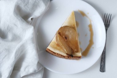 New York cheesecake Karamelize armut ile hizmet vermiştir. Beyaz plaka üzerinde yaban çiçekleri ve beyaz keten bez ile süslenmiş cheesecake