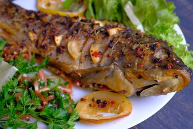 Limon, sarımsak, baharat ve otlar ile fırında pişmiş balık. Carp bir plaka üzerinde yeşillikler ile hizmet