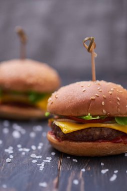 İki Amerikan cheeseburger, peynirli ve sebzeli. Koyu ahşap masada Hamburgerler.