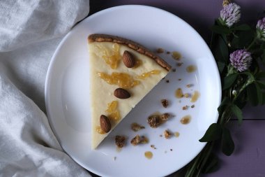 Badem ve karamel ile New York cheesecake bir dilim, beyaz bir tatlı plaka üzerinde hizmet vermiştir. Beyaz bir arka planda cheesecake, yaban çiçekleri ve keten bez ile süslenmiş