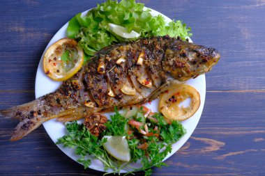 Limon, sarımsak, baharat ve otlar ile fırında pişmiş balık. Carp bir plaka üzerinde yeşillikler ile hizmet