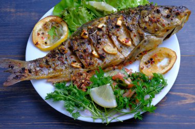 Limon, sarımsak, baharat ve otlar ile fırında pişmiş balık. Carp bir plaka üzerinde yeşillikler ile hizmet