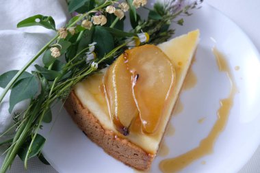 New York cheesecake Karamelize armut ile hizmet vermiştir. Beyaz plaka üzerinde yaban çiçekleri ve beyaz keten bez ile süslenmiş cheesecake