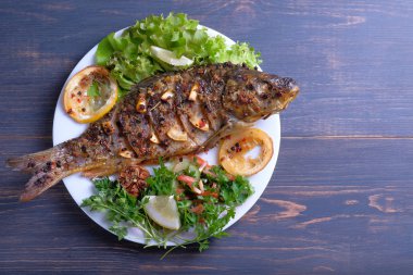 Limon, sarımsak, baharat ve otlar ile fırında pişmiş balık. Carp bir plaka üzerinde yeşillikler ile hizmet